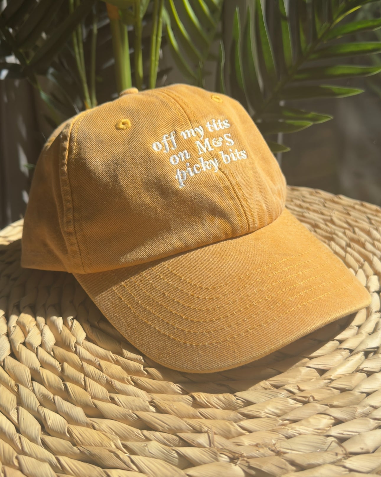 Yellow cap with text on a woven surface with greenery in the background